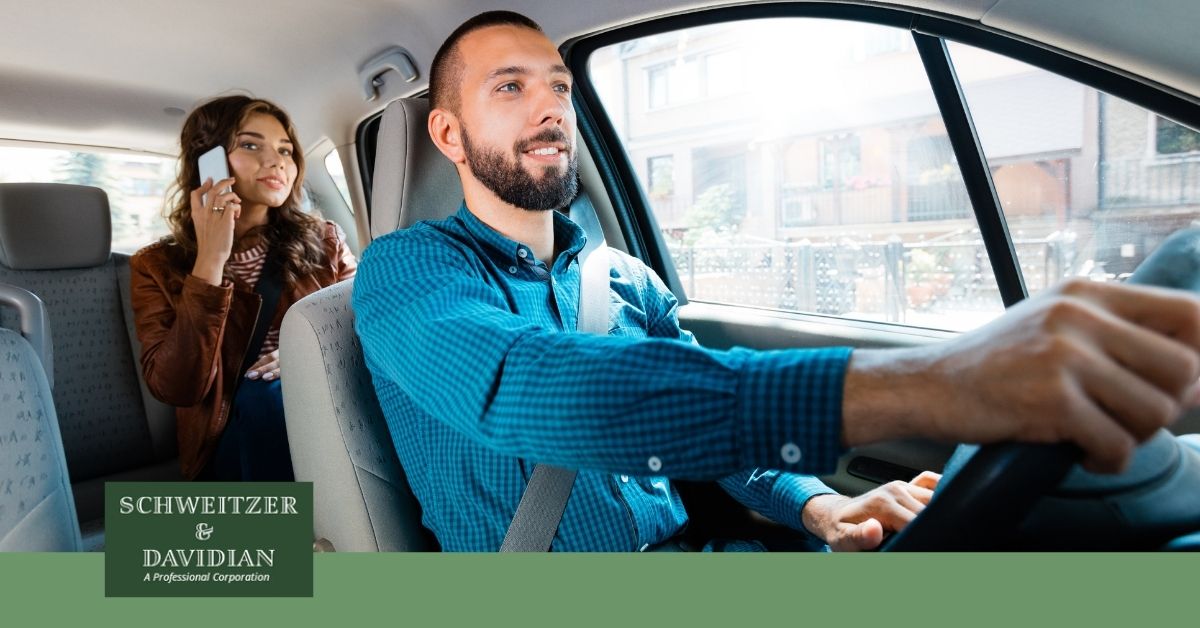 man driving with woman on phone in backseat