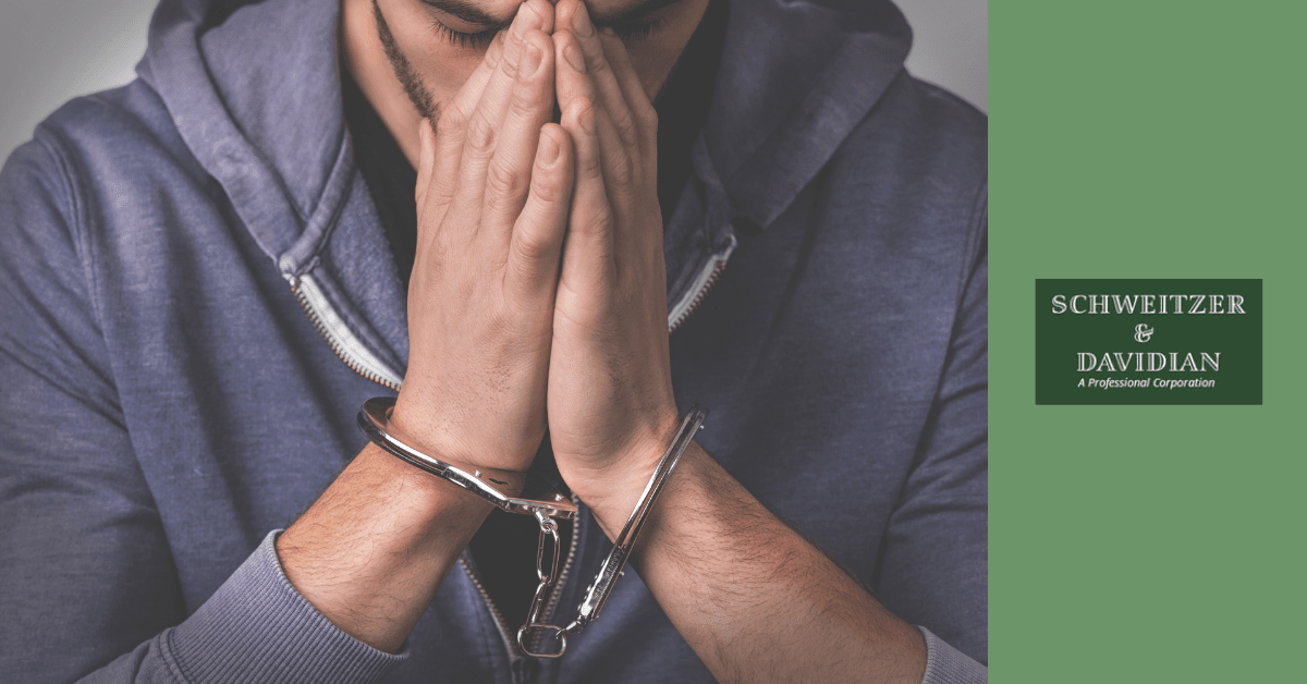 man in handcuffs covering face and looking down